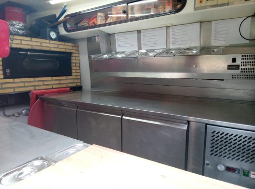 Intérieur d'un camion de restauration avec un plan de travail en acier et des équipements.